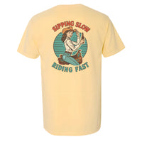 Retro western graphic t-shirt with cowgirl illustration and bold text that reads 'Sipping Slow, Riding Fast' printed on the  Butter Comfort Colors pocket tee.