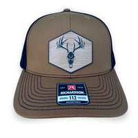 Front view of a caramel color rustic pines outfitters hat featuring an acrylic patch with a wood grain pattern and a European skull mount of a whitetail buck deer.