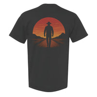 Sunset cowboy Western graphic t-shirt featuring a black silhouette of a cowboy walking away from a glowing sunset, printed on a Comfort Colors garment-dyed unisex tee with a relaxed fit.
