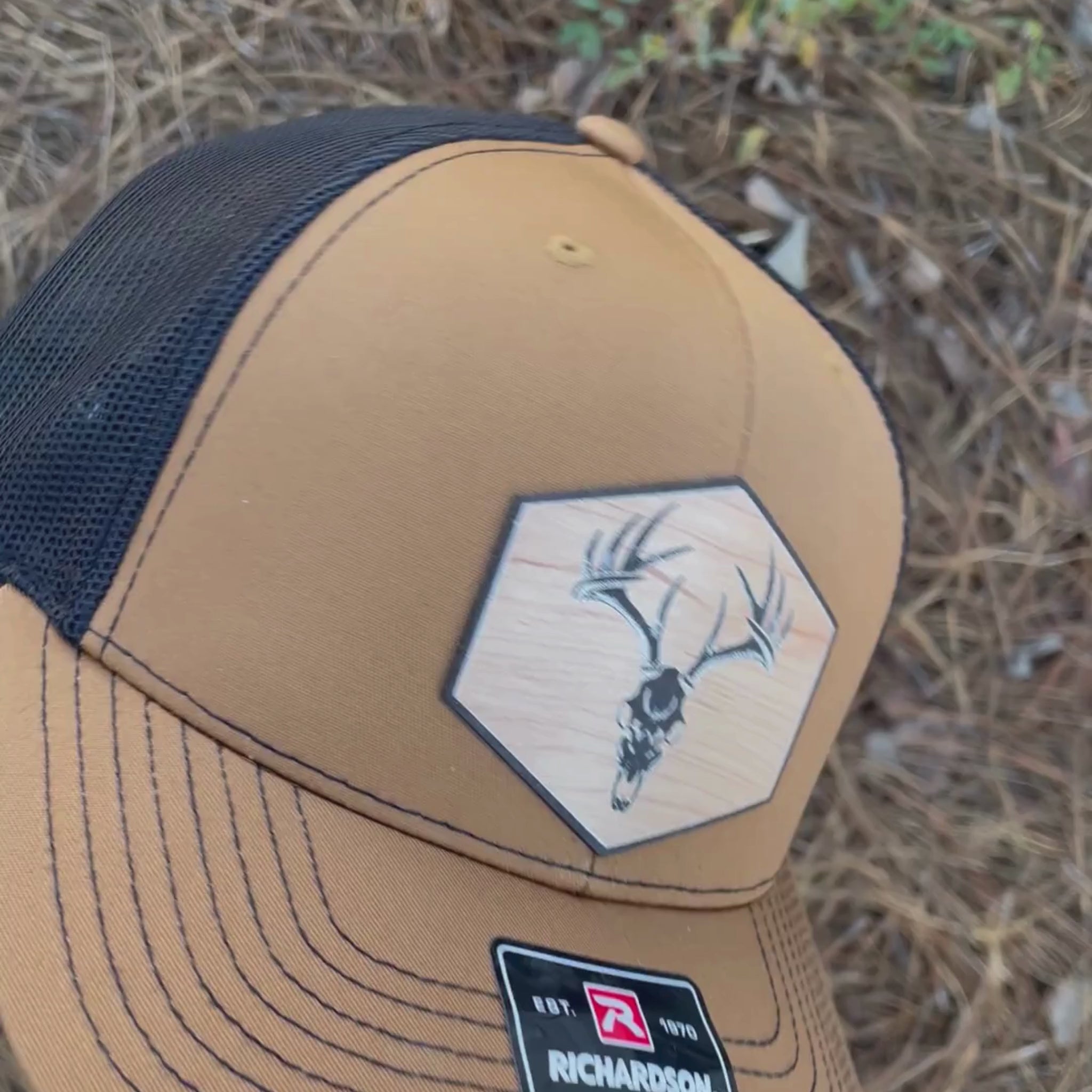 Video of a caramel color rustic pines outfitters hat featuring an acrylic patch with a wood grain pattern and a European skull mount of a whitetail buck deer.